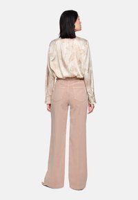 Leichte florale Bluse mit langen Ärmeln, cremigem Hintergrund und zarten pfirsichfarbenen Blumen; kombiniert mit hoch taillierten, weit geschnittenen beigen Hosen.