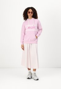 Sudadera rosa con textura estampada, logo en la parte delantera, acentos blancos, combinada con una falda larga rayada de color rosa claro. Completado con zapatillas.