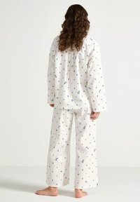Gestructureerde witte pyjama-set met blauwe bloemenpatronen. Heeft lange mouwen en wide-leg broeken, gemaakt van zachte, lichte stof.