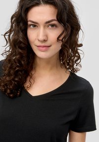 Czarny t-shirt z dekoltem w serek, wykonany z miękkiego materiału, z krótkimi rękawami i luźnym krojem, z widocznymi przeszyciami i gładką teksturą.