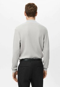 Suéter de canalé gris claro con un cuello alto, combinado con pantalones de traje negros y un cinturón texturizado. El suéter tiene mangas largas.