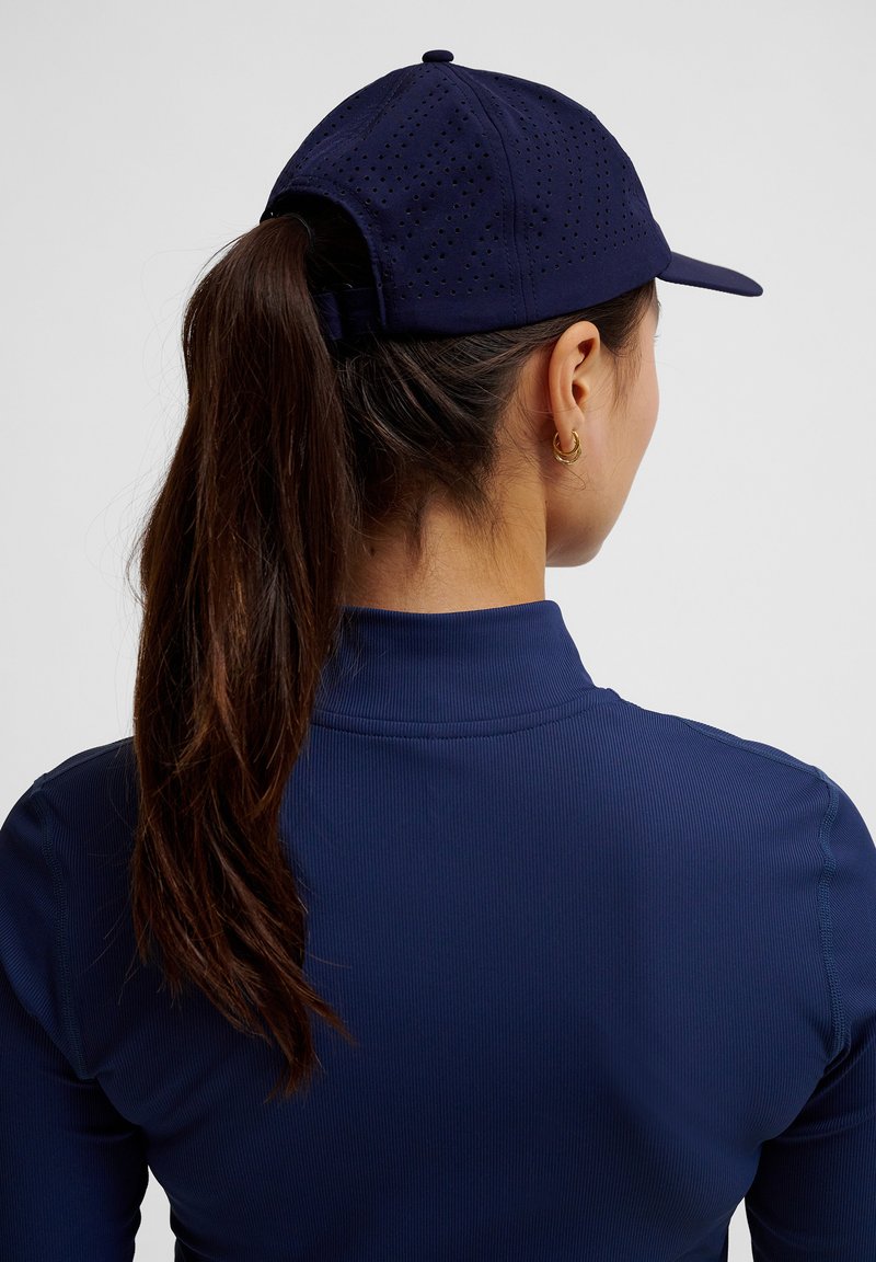 Marinblå baseballkeps med perforerat mönster, justerbar rem bak, bärs med en matchande marinblå långärmad topp.