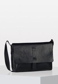 Sac en cuir noir de type messager avec une fermeture à rabat et une bandoulière ajustable. Il présente une texture lisse et un design minimaliste sans matériel visible.