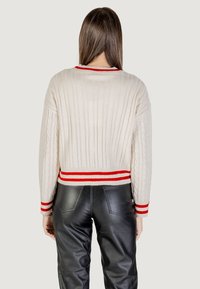 Maglione a trecce di colore crema con strisce rosse e bianche a coste all'orlo e ai polsini, abbinato a pantaloni di pelle nera.