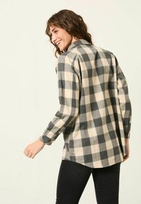 Plaid shirt in cream and dark gray, featuring long sleeves, a collar, and a loose fit. Back view shows buttoned cuffs and side slits.