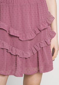 Jupe rose à volants en tissu léger avec des pois texturés. Elle présente trois niveaux de volants le long de l'ourlet pour un détail supplémentaire.