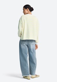 Gelb-weiß gestreifter, übergroßer Pullover mit herabgesetzten Schultern, kombiniert mit lockeren, hellblauen Jeans und beigen Schuhen.