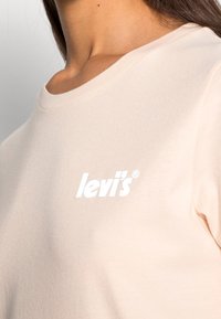 Jasnoróżowa bawełniana koszulka z okrągłym dekoltem i białym, nadrukowanym logo "levi's" na piersi. Miękka tekstura, prosty design bez wzorów.