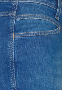 Tejido de mezclilla azul que muestra un primer plano de un área de bolsillo, con una textura suave, costuras en contraste y un diseño limpio y clásico.