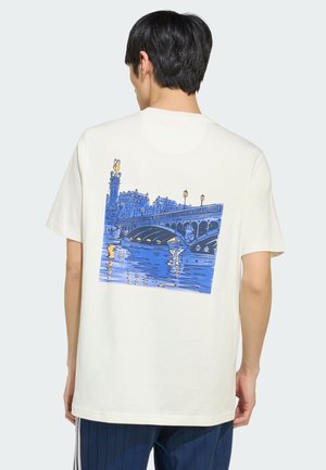 Junger Mann trägt weißes T-Shirt mit blauem Motiv einer europäischen Brücke über Wasser, gesehen von hinten.