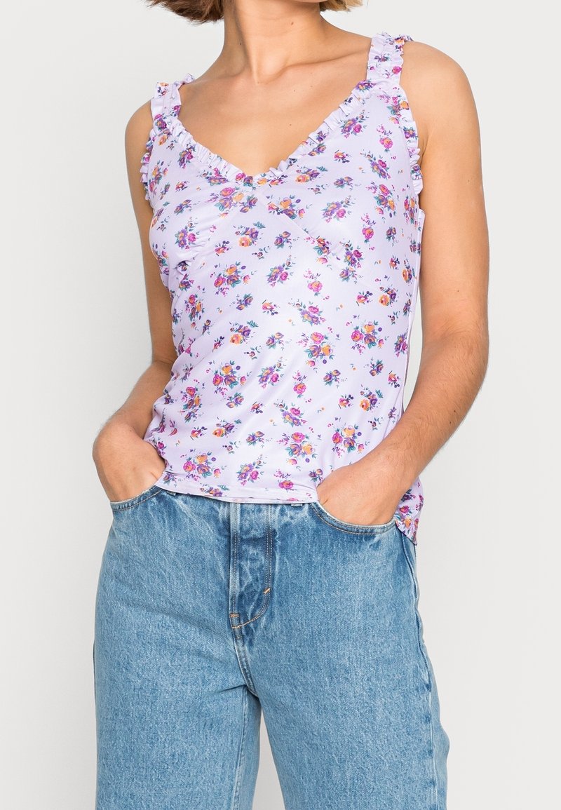 Débardeur floral lavande avec bretelles à volants et encolure en V, fabriqué en tissu léger ; assorti à un jean taille haute bleu clair.
