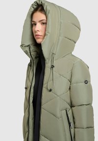 Lys grøn oppustelig jakke med en stor hætte, diamantquiltet design, snoretræk og lynlåslommer på siden. Glat overflade.