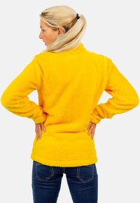 Geel fleece pullover met een zachte, gestructureerde oppervlakte, lange mouwen en een relaxte pasvorm, gedragen over donkere spijkerbroek.
