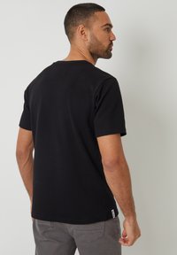 Camiseta negra de manga corta hecha de tejido acanalado, con cuello redondo y una pequeña etiqueta de logo en el lado inferior.