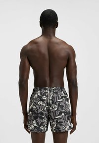 Patronen badshorts in grijs met zwart bloemenpatroon, elastische tailleband en contrasterende stiksels. De stof lijkt lichtgewicht en soepel te zijn.