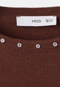 Collo di un maglione lavorato a maglia marrone con dettagli in occhio di bue argentati e etichetta bianca che mostra la taglia piccola per EUR-USA e MEX.