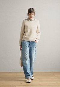 Pull crème avec une finition texturée, jean en denim bleu clair et chaussures blanches. Accessoire : sac à main beige. Col simple avec des embellissements.