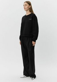 Hanorac negru cu guler rotund și un mic text gri „oui” imprimat pe piept, asortat cu pantaloni largi cu dungi negri și pantofi argintii.