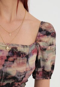 Monivärinen pusero neliönmuotoisella kaula-aukolla, puffihihoilla ja teksturoidulla kankaalla, jossa on abstrakteja kuvioita pinkissä, vihreässä ja mustassa.