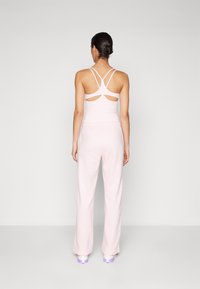 Light pink athletic top with cross-back straps and cut-out details, paired with light pink, loose-fitting pants and white shoes with purple accents.