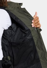 Grüne Kapuzenjacke mit einem Reißverschluss an der Vorderseite, mit glattem Äußeren, strukturiertem schwarzen Innenfutter und einer Netz-Tasche.