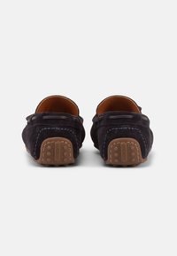 Ζευγάρι από ναυτικό σουέτ μοκασίνια, εμφανιζόμενα από πίσω, με τακούνια από καφέ καουτσούκ με στύλωμα για τράβηγμα και ανάλογες λεπτομέρειες ραψίματος σε ναυτικό χρώμα.