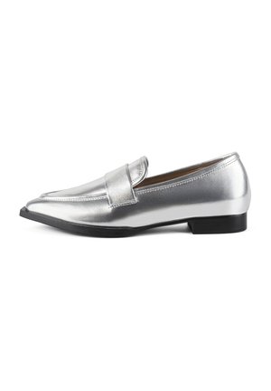 Mocasines plateados metálicos con punta afilada, suela plana negra y una correa decorativa. Textura suave y diseño elegante.