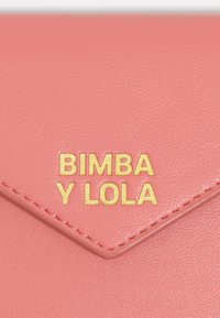 Różowy skórzany portfel z złotym napisem "Bimba y Lola". Cechuje się gładką fakturą i zapięciem w stylu koperty z przeszytymi krawędziami.