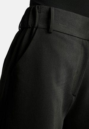 Close-up of black pants with an elastic waistband, belt loops, side pocket, and smooth fabric texture.