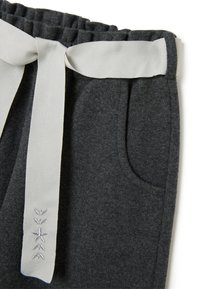 Un pantalon en mélange de laine gris présente une taille élastique avec une cordon blanche contrastante. Des poches latérales et de délicites coutures décoratives sont visibles.