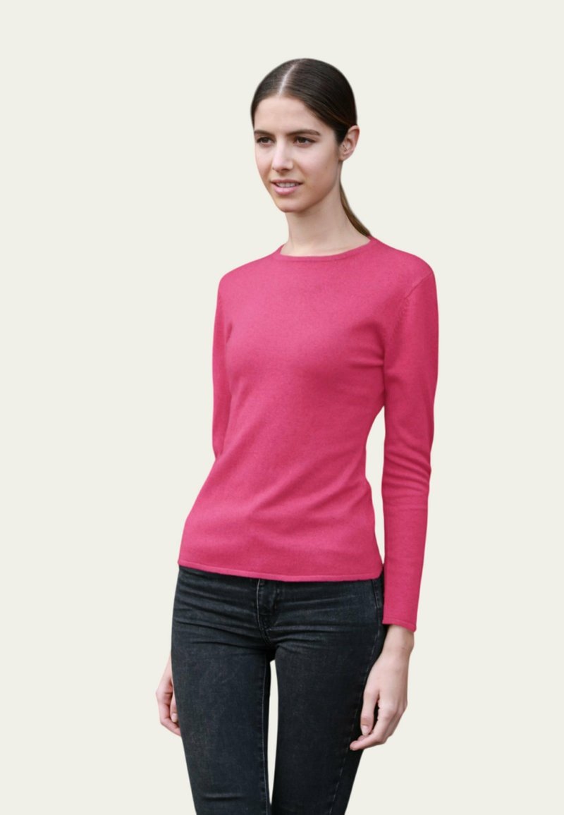 Pull long à manches longues rose ajusté en tricot lisse et doux. Associé à un jean en denim foncé, avec un col rond et une silhouette près du corps.
