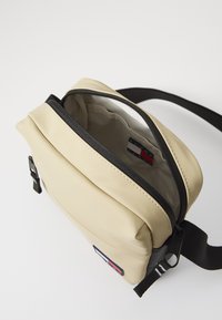 Borsa a tracolla beige realizzata in materiale liscio, con zip nera, tracolla regolabile e fodera interna con etichetta del logo.