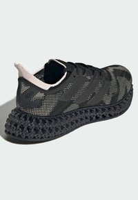Zapatilla deportiva negra y beige con parte superior de malla, tres rayas negras y suela estructurada en 3D con diseño de rejilla sobre un fondo blanco.