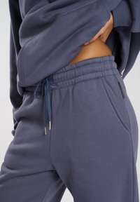 Donkergrijze, zachte joggingbroeken van stof met een elastieken tailleband, trekkoord en zijzakken. Heeft een slim fit en een gladde textuur.