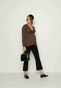 Blusa de maternidade em estilo envelope com fundo castanho e padrão floral pequeno, acompanhada de calças pretas curtas. Acessorizada com uma bolsa preta e sapatos.
