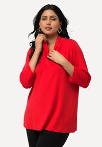 Punainen pullover-paita, jossa on kauluskotelo ja kolme neljäsosaa hihat, jossa on sileä tekstuuri ja rento, virtaava istuvuus.