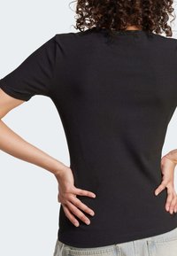 Czarny t-shirt z prążkowanej tkaniny, o dopasowanym kroju, z krótkimi rękawami i okrągłym dekoltem, połączony z jasnymi szortami dżinsowymi.