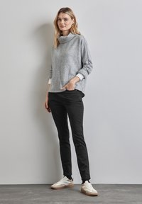 Grå stickad tröja i ullblandning med cowl-neck, långa ärmar och öppna sidor, tillsammans med svarta slim-fit byxor och vita sneakers med beige detaljer.