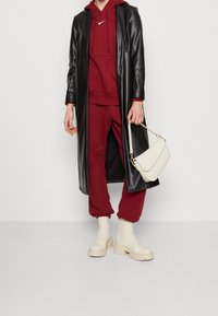 Black faux leather long coat, maroon hoodie, matching sweatpants, cream bag, and beige platform boots. Sleek textures with minimal accents.