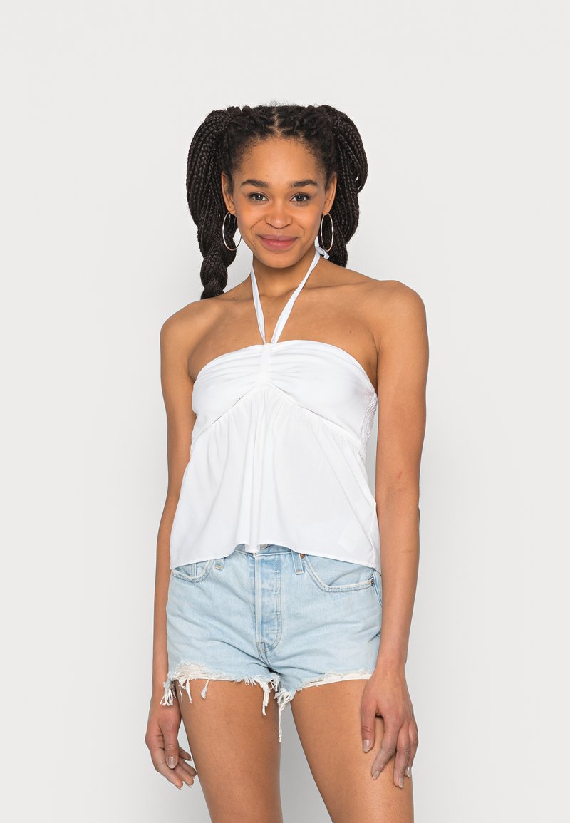 Top halter branco com tecido franzido na zona do busto, material leve e alças ajustáveis. Combinado com calções de ganga claros.
