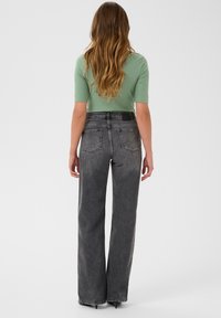 Top verde a coste con maniche corte abbinato a jeans neri sbiaditi a vita alta e gamba larga, con tasche posteriori e finitura in tessuto testurizzato.