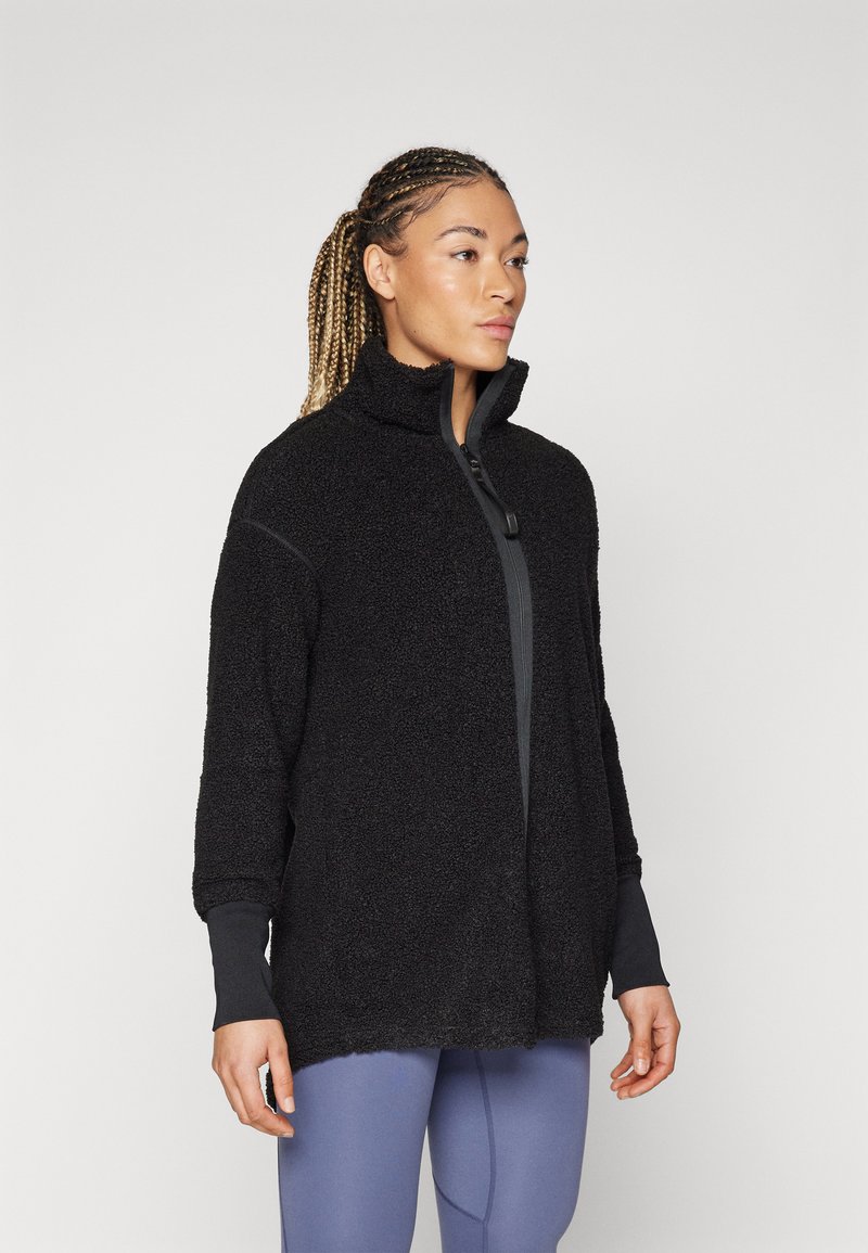 Black fleece jacket with high collar, zip closure, and textured fabric. Features long sleeves and a relaxed fit. Paired with light blue leggings.