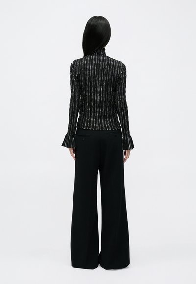 Jachetă neagră cu mâneci lungi și dungi verticale, cu guler înalt, asortată cu pantaloni negri cu picioare largi, având manșete largi și material texturat.