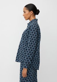 Camicia blu navy con grandi pois a contrasto. Design con bottoni, taschino sul petto, vestibilità comoda. Tessuto morbido con una consistenza liscia.