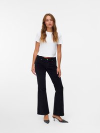Pantalons évasés noirs en tissu doux, associés à un crop top blanc ajusté. Les chaussures présentent un design à pois noir et blanc avec un bout pointu.