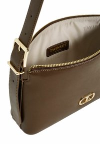 Borsa a tracolla in pelle marrone con hardware dorato, chiusura con zip e fodera beige che presenta il logo "TWISTSET". Texture liscia e forma rettangolare.