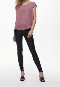 Blusa rosa a maniche corte abbinata a pantaloni in similpelle neri aderenti e tacchi aperti neri, creando una silhouette elegante.