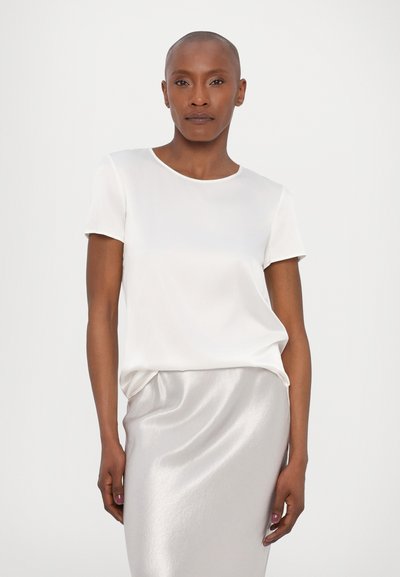 Blusa branca de manga curta com decote redondo, feita de um tecido suave. Combinada com uma saia midi prateada brilhante.