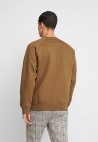 Brun sweatshirt med rund halsringning och ribbade muddar. Mjuk textur, avslappnad passform, matchad med rutiga byxor med orange och svarta accenter.