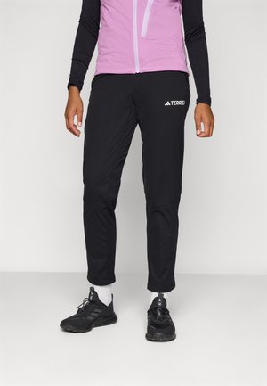 Sorte treningbukser med en tapered passform, med et teksturert mønster på den nederste delen av benet og "TERREX" logoen. Kombinert med svarte joggesko.